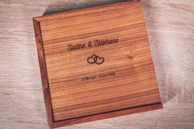Coffret en bois foncé gravé aux prénoms des mariés posé sur une table